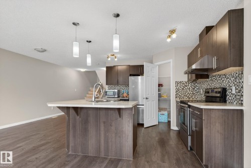 Kitchen with stainless steel appliances, dark brown cabinetry, pendant lighting, decorative backsplash, and under cabinet range hood - 1717 Chapman Way, Edmonton, AB - Indoor Photo Showing Kitchen With Upgraded Kitchen