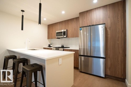 Kitchen with stainless steel appliances, a kitchen bar, modern cabinets, a peninsula, and decorative light fixtures - 11738 91 Street Nw, Edmonton, AB - Indoor Photo Showing Kitchen