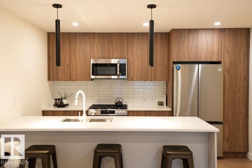 Kitchen with a kitchen bar, modern cabinets, wood finish cabinets, and stainless steel appliances - 11738 91 Street Nw, Edmonton, AB - Indoor Photo Showing Kitchen With Upgraded Kitchen