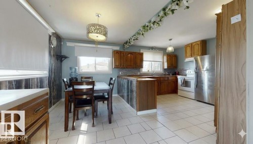 Kitchen with wood finish cabinets, hanging light fixtures, freestanding refrigerator, white range with electric stovetop, and a peninsula - 4706 53 St, Leduc, AB - Indoor