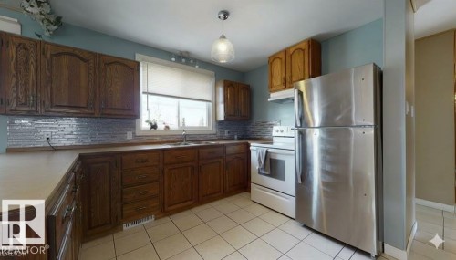 Kitchen featuring freestanding refrigerator, white electric range oven, light tile patterned flooring, light countertops, and wood finish cabinets - 4706 53 St, Leduc, AB - Indoor Photo Showing Kitchen With Double Sink