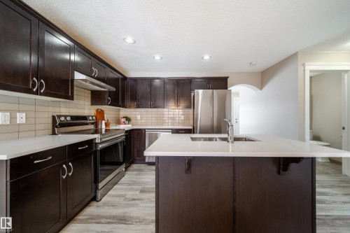 Kitchen featuring stainless steel appliances, dark wood finish cabinets, a center island with sink, arched walkways, and light wood-style flooring - 2919 15 Street, Edmonton, AB - Indoor Photo Showing Kitchen With Double Sink With Upgraded Kitchen