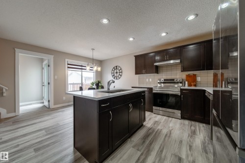 Kitchen with stainless steel appliances, a kitchen island with sink, hanging lights, light wood finished floors, and a textured ceiling - 2919 15 Street, Edmonton, AB - Indoor Photo Showing Kitchen With Double Sink
