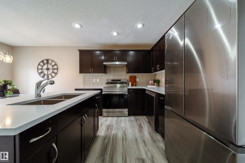 Kitchen featuring stainless steel appliances, a kitchen island with sink, light wood-style floors, backsplash, and a textured ceiling - 2919 15 Street, Edmonton, AB - Indoor Photo Showing Kitchen With Double Sink With Upgraded Kitchen