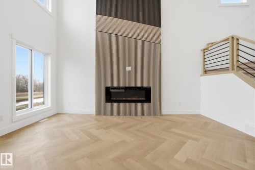 Unfurnished living room featuring an accent wall, plenty of natural light, parquet flooring, a high ceiling, and a glass covered fireplace - 3294 Chernowski Way, Edmonton, AB - Indoor Photo Showing Living Room With Fireplace