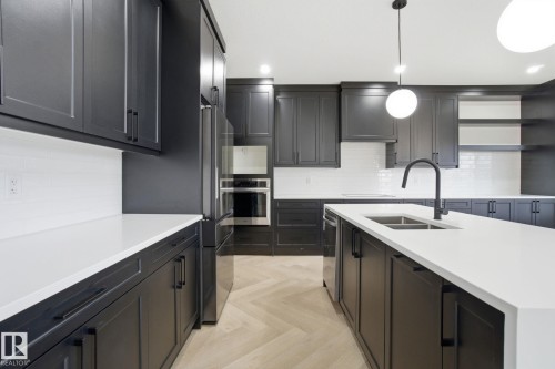 Kitchen with light stone countertops, stainless steel appliances, parquet floors, and backsplash - 3294 Chernowski Way, Edmonton, AB - Indoor Photo Showing Kitchen With Double Sink With Upgraded Kitchen