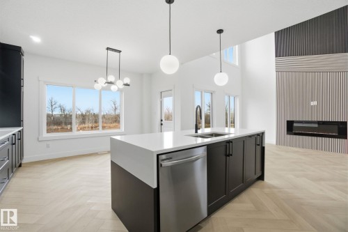 Kitchen featuring a kitchen island with sink, parquet floors, a glass covered fireplace, and stainless steel dishwasher - 3294 Chernowski Way, Edmonton, AB - Indoor Photo Showing Kitchen With Double Sink With Upgraded Kitchen
