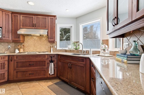 Kitchen with light stone counters, light tile patterned floors, stainless steel dishwasher, wood finish cabinets, and recessed lighting - 326 O'Connor Close, Edmonton, AB - Indoor Photo Showing Kitchen
