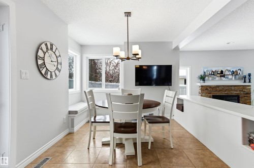 Dining room featuring plenty of natural light, suspended lighting, a stone fireplace, a textured ceiling, and light tile patterned floors - 326 O'Connor Close, Edmonton, AB - Indoor Photo Showing Dining Room