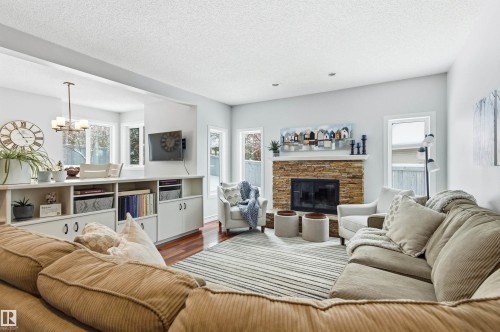 Living room with wood finished floors, a chandelier, a stone fireplace, and a textured ceiling - 326 O'Connor Close, Edmonton, AB - Indoor Photo Showing Living Room With Fireplace