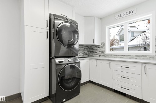 Laundry room featuring stacked washer / dryer, light tile patterned floors, cabinet space, and a textured ceiling - 326 O'Connor Close, Edmonton, AB - Indoor Photo Showing Laundry Room