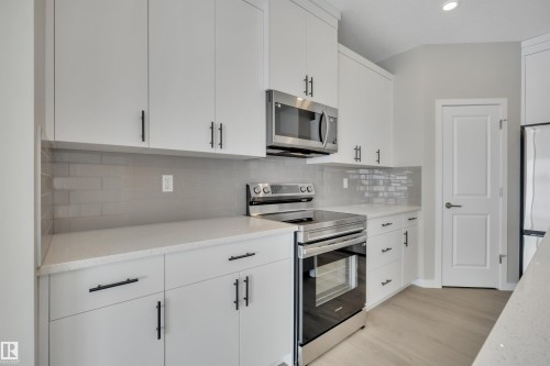 Kitchen featuring stainless steel appliances, white cabinets, backsplash, light wood-style floors, and light stone countertops - 5657 Hawthorn Way, Edmonton, AB - Indoor Photo Showing Kitchen