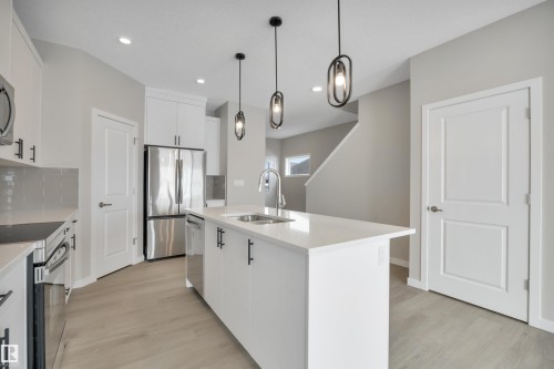 Kitchen featuring white cabinets, a kitchen island with sink, stainless steel appliances, light wood-style flooring, and decorative light fixtures - 5657 Hawthorn Way, Edmonton, AB - Indoor Photo Showing Kitchen With Stainless Steel Kitchen With Double Sink With Upgraded Kitchen