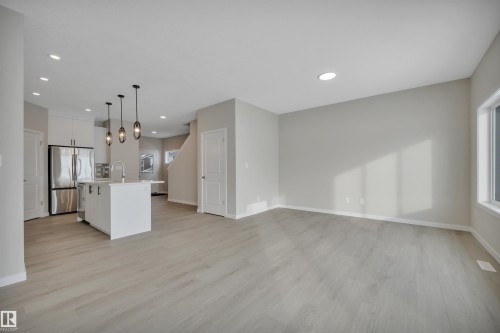 Kitchen featuring a kitchen island with sink, open floor plan, white cabinets, freestanding refrigerator, and light wood-style floors - 5657 Hawthorn Way, Edmonton, AB - Indoor