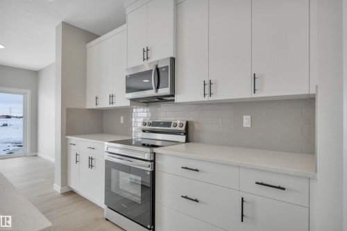 Kitchen with stainless steel appliances, white cabinets, tasteful backsplash, light stone countertops, and light wood-type flooring - 5657 Hawthorn Way, Edmonton, AB - Indoor Photo Showing Kitchen