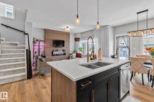 Kitchen with dark cabinetry, pendant lighting, open floor plan, light stone counters, and an island with sink - 324 41 Street, Edmonton, AB - Indoor Photo Showing Kitchen With Double Sink