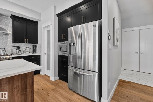 Kitchen with dark cabinets, stainless steel appliances, light stone countertops, tasteful backsplash, and light wood-style floors - 324 41 Street, Edmonton, AB - Indoor Photo Showing Kitchen