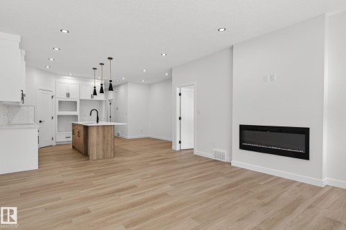Two tone kitchen featuring open floor plan, an island with sink, two tone cabinetry, a glass covered fireplace, and pendant lighting - 3318 Chickadee Drive, Edmonton, AB - Indoor With Fireplace