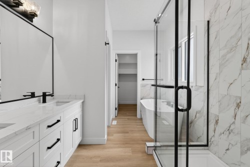 Bathroom featuring a marble finish shower, a freestanding tub, double vanity, a spacious closet, and light wood-type flooring - 3318 Chickadee Drive, Edmonton, AB - Indoor