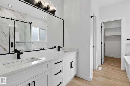 Bathroom featuring a marble finish shower, double vanity, a soaking tub, a spacious closet, and light wood-style floors - 3318 Chickadee Drive, Edmonton, AB - Indoor