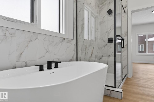Full bath featuring a marble finish shower, a freestanding bath, and light wood finished floors - 3318 Chickadee Drive, Edmonton, AB - Indoor Photo Showing Bathroom