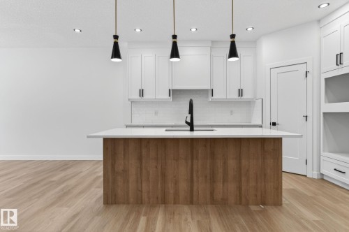 Dual tone kitchen with a kitchen island with sink, decorative light fixtures, light wood-style flooring, light stone counters, and two tone color scheme - 3318 Chickadee Drive, Edmonton, AB - Indoor Photo Showing Kitchen