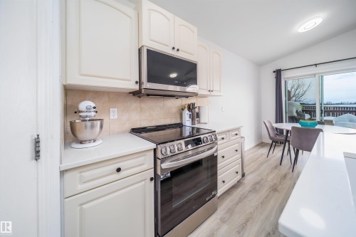 Kitchen featuring stainless steel appliances, decorative backsplash, vaulted ceiling, light wood-style flooring, and white cabinets - 1179 Oakland Drive, Devon, AB - Indoor Photo Showing Kitchen