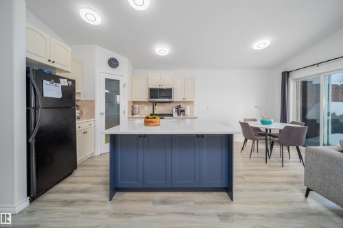 Kitchen featuring freestanding refrigerator, a center island with sink, two tone cabinetry, decorative backsplash, and light wood-style floors - 1179 Oakland Drive, Devon, AB - Indoor Photo Showing Kitchen
