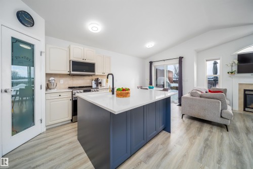 Kitchen featuring stainless steel appliances, two tone cabinets, open floor plan, light wood-style floors, and an island with sink - 1179 Oakland Drive, Devon, AB - Indoor Photo Showing Kitchen With Fireplace