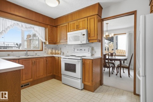 Kitchen with white appliances, wood finish cabinetry, light countertops, hanging lights, and backsplash - 65 Lorne Crescent, St. Albert, AB - Indoor Photo Showing Kitchen