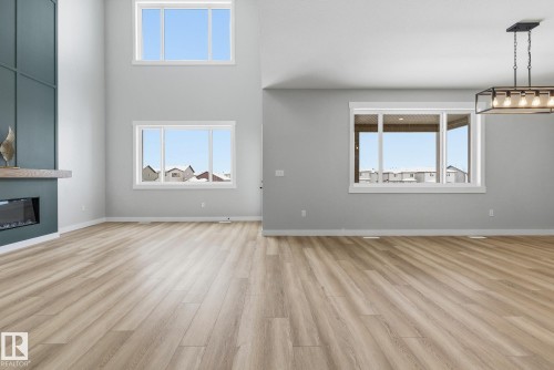 Unfurnished living room with a fireplace, light wood-style flooring, plenty of natural light, a high ceiling, and suspended lighting - 28 Harley Way, Spruce Grove, AB - Indoor With Fireplace
