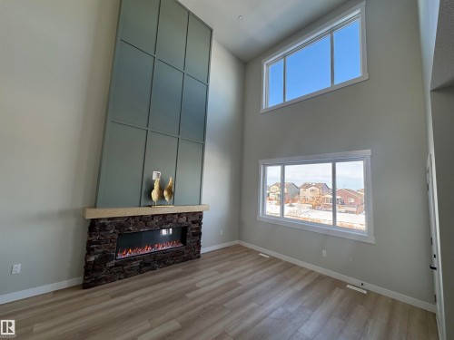 Unfurnished living room with a stone fireplace, light wood finished floors, a high ceiling, and plenty of natural light - 28 Harley Way, Spruce Grove, AB - Indoor With Fireplace
