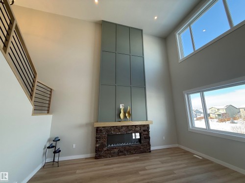 Unfurnished living room with plenty of natural light, light wood finished floors, a stone fireplace, a high ceiling, and recessed lighting - 28 Harley Way, Spruce Grove, AB - Indoor Photo Showing Other Room With Fireplace