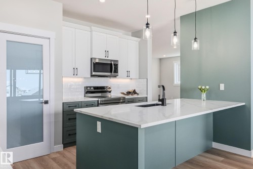 Dual tone kitchen featuring dual tone cabinets, stainless steel appliances, pendant lighting, light wood-style floors, and backsplash - 28 Harley Way, Spruce Grove, AB - Indoor Photo Showing Kitchen With Upgraded Kitchen