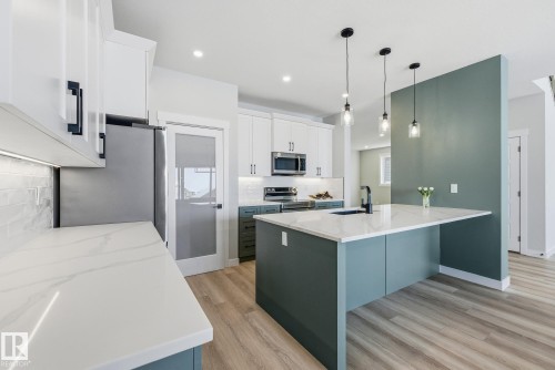Kitchen with two tone cabinetry, hanging light fixtures, light wood-style floors, stainless steel appliances, and light stone countertops - 28 Harley Way, Spruce Grove, AB - Indoor Photo Showing Kitchen With Upgraded Kitchen