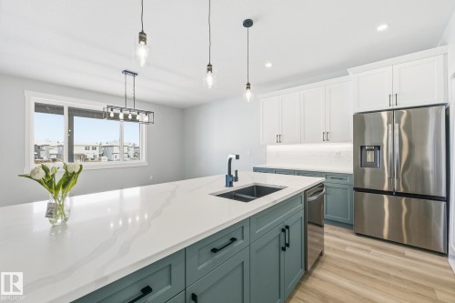 Dual tone kitchen featuring two tone cabinets, stainless steel appliances, pendant lighting, light wood-type flooring, and light stone counters - 28 Harley Way, Spruce Grove, AB - Indoor Photo Showing Kitchen With Double Sink With Upgraded Kitchen