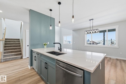 Kitchen featuring stainless steel dishwasher, decorative light fixtures, light wood-style floors, and light stone countertops - 28 Harley Way, Spruce Grove, AB - Indoor Photo Showing Kitchen With Double Sink With Upgraded Kitchen