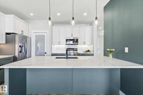 Dual tone kitchen with two tone color scheme, decorative backsplash, stainless steel appliances, decorative light fixtures, and light stone countertops - 28 Harley Way, Spruce Grove, AB - Indoor Photo Showing Kitchen With Upgraded Kitchen