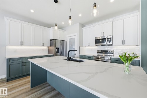 Dual tone kitchen featuring two tone color scheme, pendant lighting, stainless steel appliances, backsplash, and light wood-style flooring - 28 Harley Way, Spruce Grove, AB - Indoor Photo Showing Kitchen With Double Sink With Upgraded Kitchen