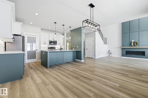 Kitchen featuring open floor plan, two tone cabinets, decorative light fixtures, stainless steel appliances, and light wood-style floors - 28 Harley Way, Spruce Grove, AB - Indoor Photo Showing Kitchen With Upgraded Kitchen