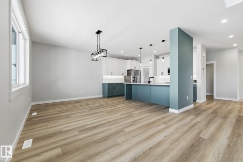 Two tone kitchen featuring open floor plan, light countertops, hanging light fixtures, light wood-type flooring, and dual tone cabinets - 28 Harley Way, Spruce Grove, AB - Indoor Photo Showing Other Room