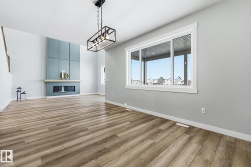 Unfurnished living room featuring light wood-style floors, a fireplace, and suspended lighting - 28 Harley Way, Spruce Grove, AB - Indoor Photo Showing Other Room With Fireplace