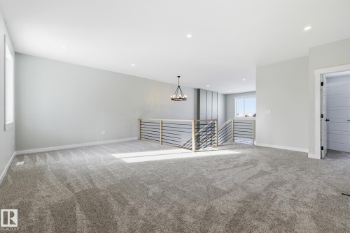 Carpeted empty room featuring baseboards and a chandelier - 28 Harley Way, Spruce Grove, AB - Indoor Photo Showing Other Room