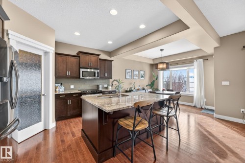 Kitchen featuring dark wood finish cabinets, light stone counters, tasteful backsplash, stainless steel appliances, and a center island with sink - 21 Dittrich, Fort Saskatchewan, AB - Indoor Photo Showing Kitchen With Double Sink With Upgraded Kitchen