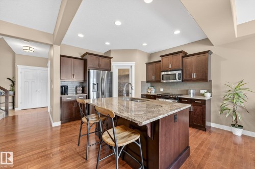Kitchen with light stone counters, decorative backsplash, stainless steel appliances, a breakfast bar area, and a center island with sink - 21 Dittrich, Fort Saskatchewan, AB - Indoor Photo Showing Kitchen With Double Sink With Upgraded Kitchen