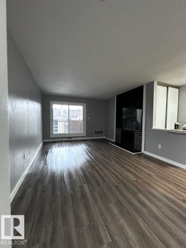 Unfurnished living room featuring a textured ceiling, dark wood-style flooring, and a tiled fireplace - 302 49 Akins Drive, St. Albert, AB - Indoor With Fireplace