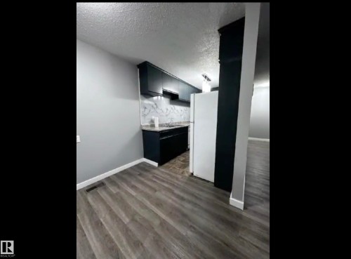 Kitchen with freestanding refrigerator, light countertops, a textured ceiling, dark cabinetry, and light wood-type flooring - 302 49 Akins Drive, St. Albert, AB - 