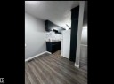 Kitchen with freestanding refrigerator, light countertops, a textured ceiling, dark cabinetry, and light wood-type flooring - 302 49 Akins Drive, St. Albert, AB  -  