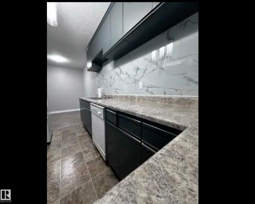 Kitchen with light countertops, white dishwasher, backsplash, a textured ceiling, and dark stone finish floors - 302 49 Akins Drive, St. Albert, AB - Indoor Photo Showing Other Room