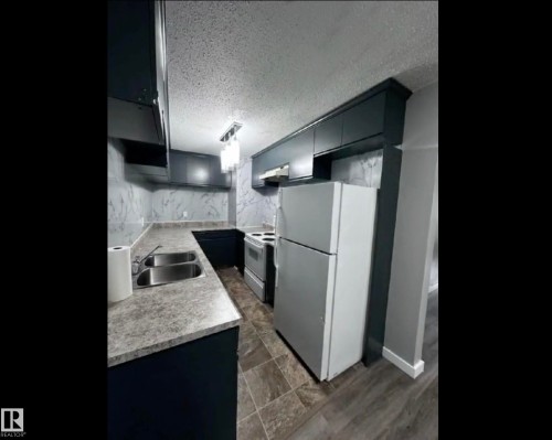 Kitchen with white appliances, light countertops, a textured ceiling, gray cabinets, and decorative light fixtures - 302 49 Akins Drive, St. Albert, AB - Indoor Photo Showing Kitchen With Double Sink